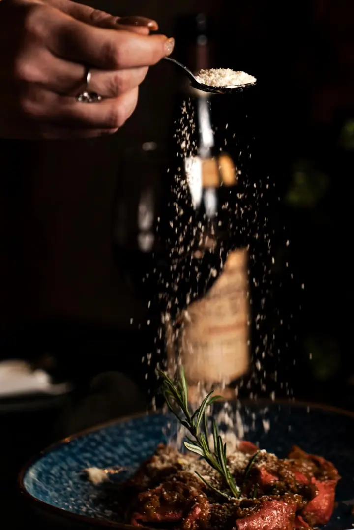 Il cucchiaio distribuisce il grana sui tortelloni all'Amarone ripieni di brasato, con rosmarino e una bottiglia di Amarone